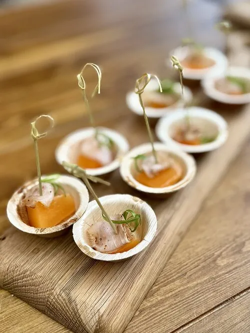 Melon and crudo bites served on small palm-leaf plates